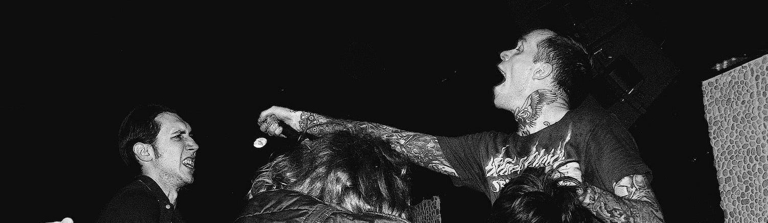 Black and white photo of the band Converge during a concert scene with a person on stage interacting with the crowd.